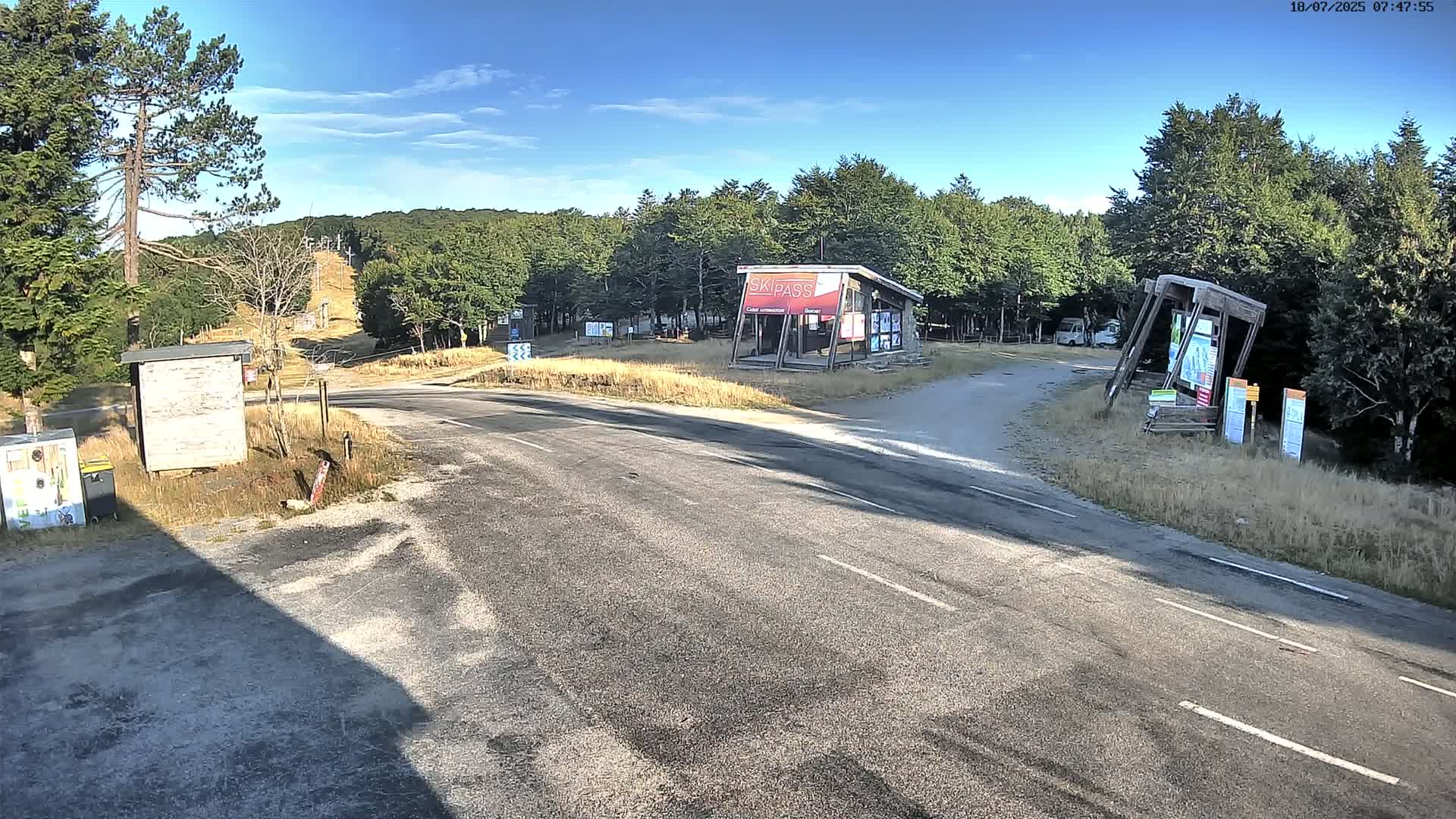 A paved road winds through a forested area on a sunny day, leading to a ski lift and several small structures.