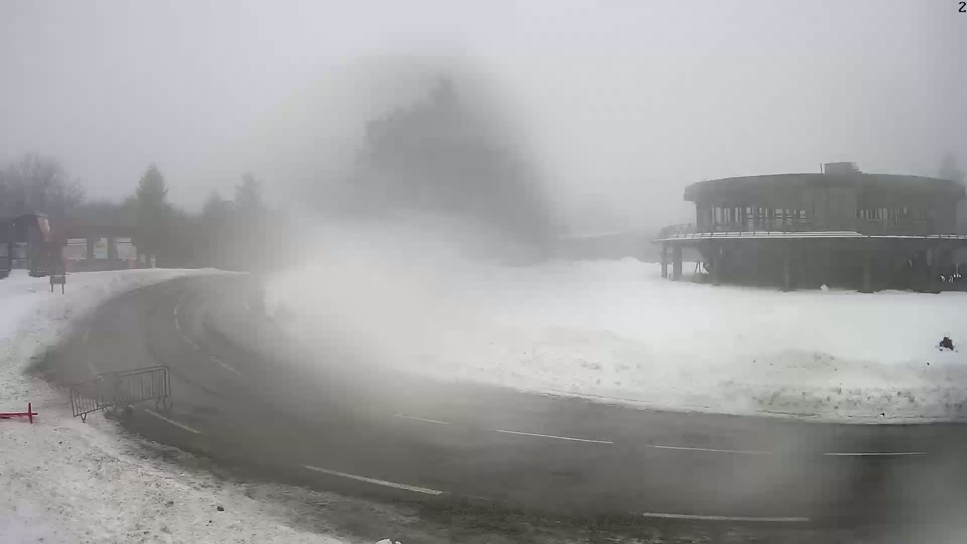 A curving road in a snowy area with a circular building in the background is obscured by thick fog.