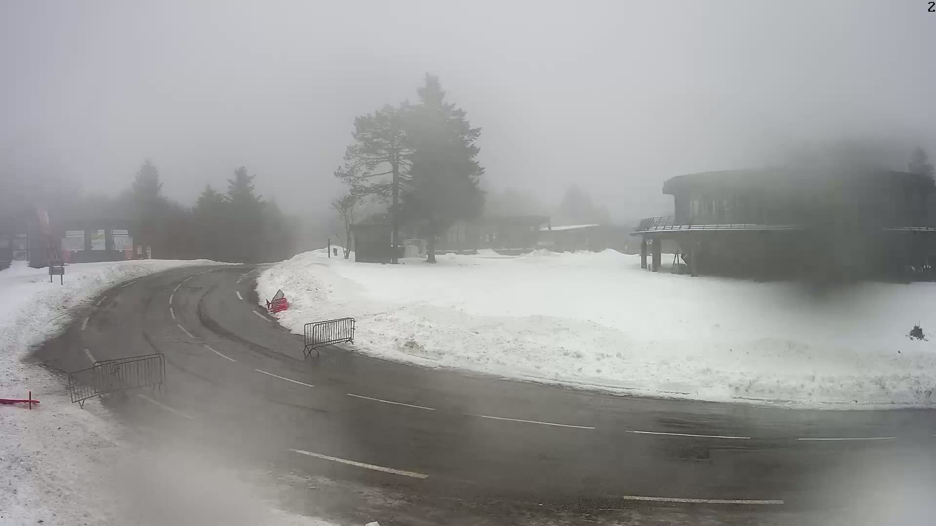 A snow-covered road curves past a building obscured by heavy fog, with metal barriers along the roadside.