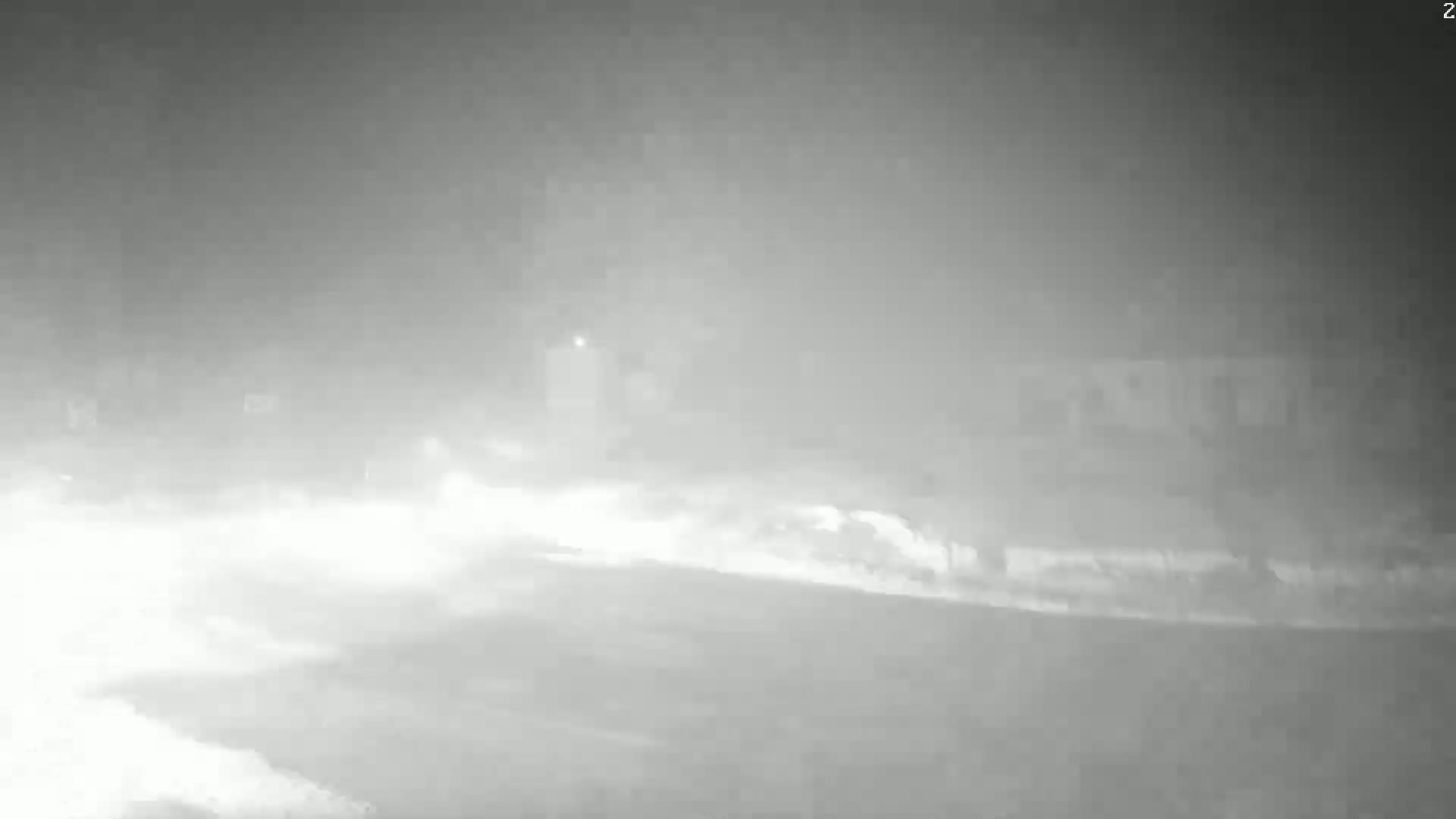 A nighttime scene shows a snowy, hazy road with faint lights and indistinct structures in the background.