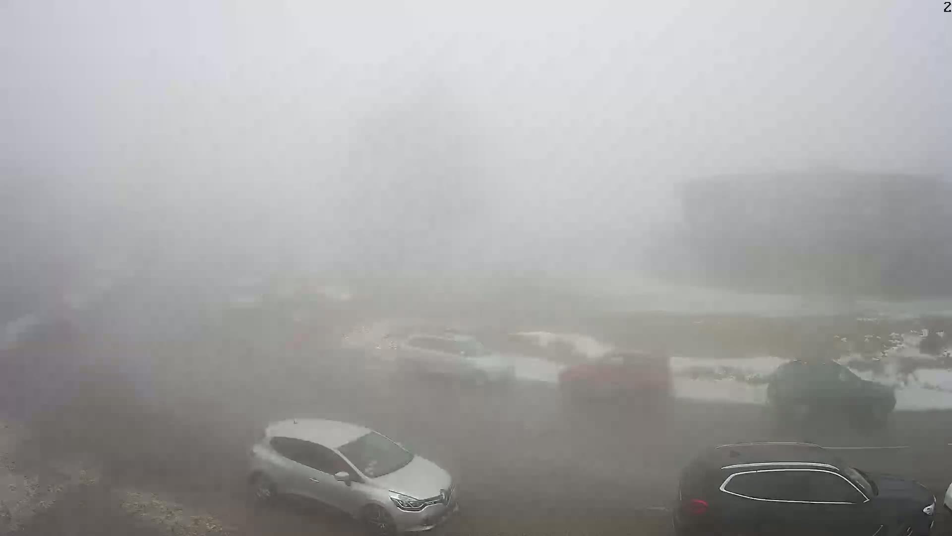 Several cars are parked and driving in a parking lot shrouded in thick fog.
