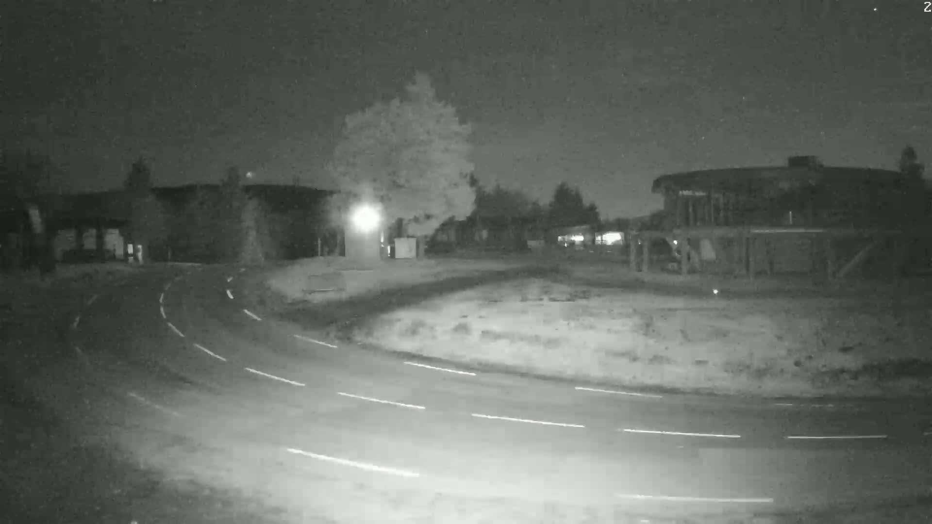 A nighttime, low-light view shows a curving roadway in front of several buildings and trees under a clear, dark sky.