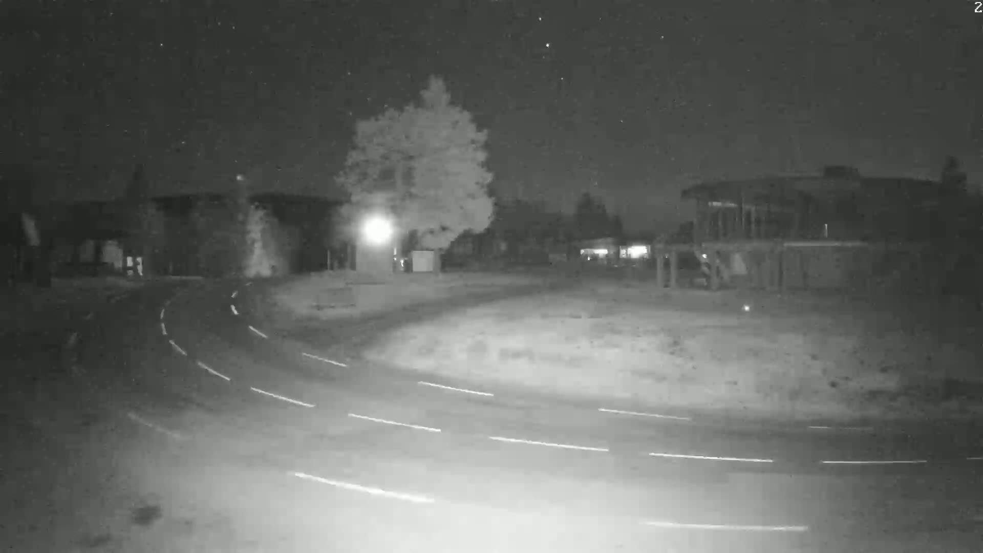 A nighttime, low-light view of a curved road leading to a building and trees under a clear, starry sky.