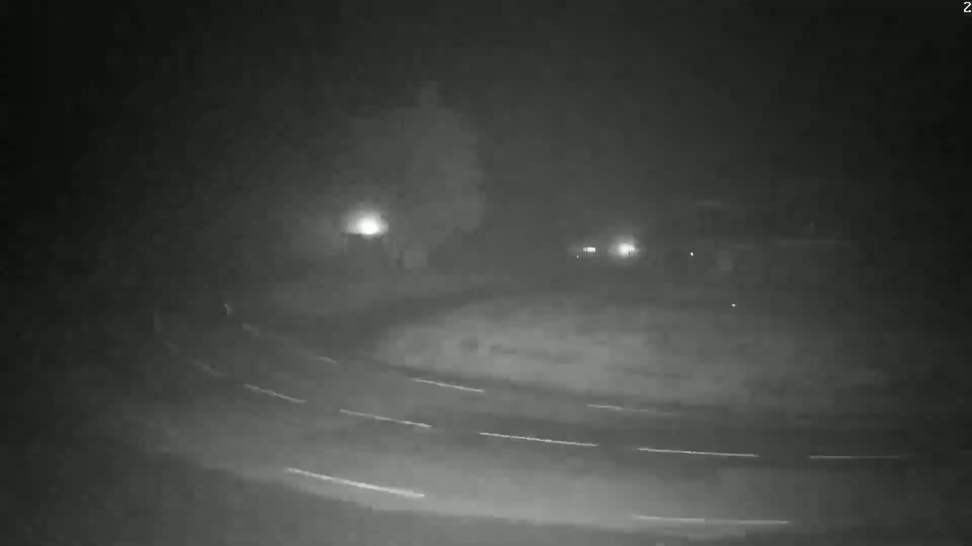 A nighttime, foggy scene shows a curved roadway with faint headlights in the distance.
