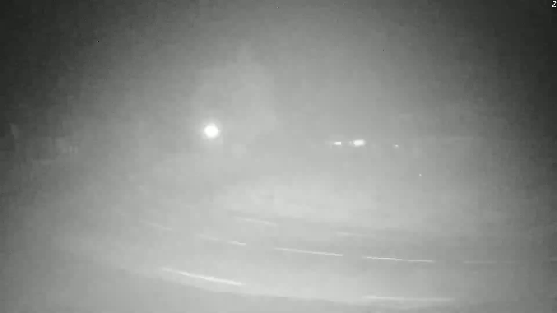 A dimly lit, foggy road is visible at night, with faint light sources in the distance.