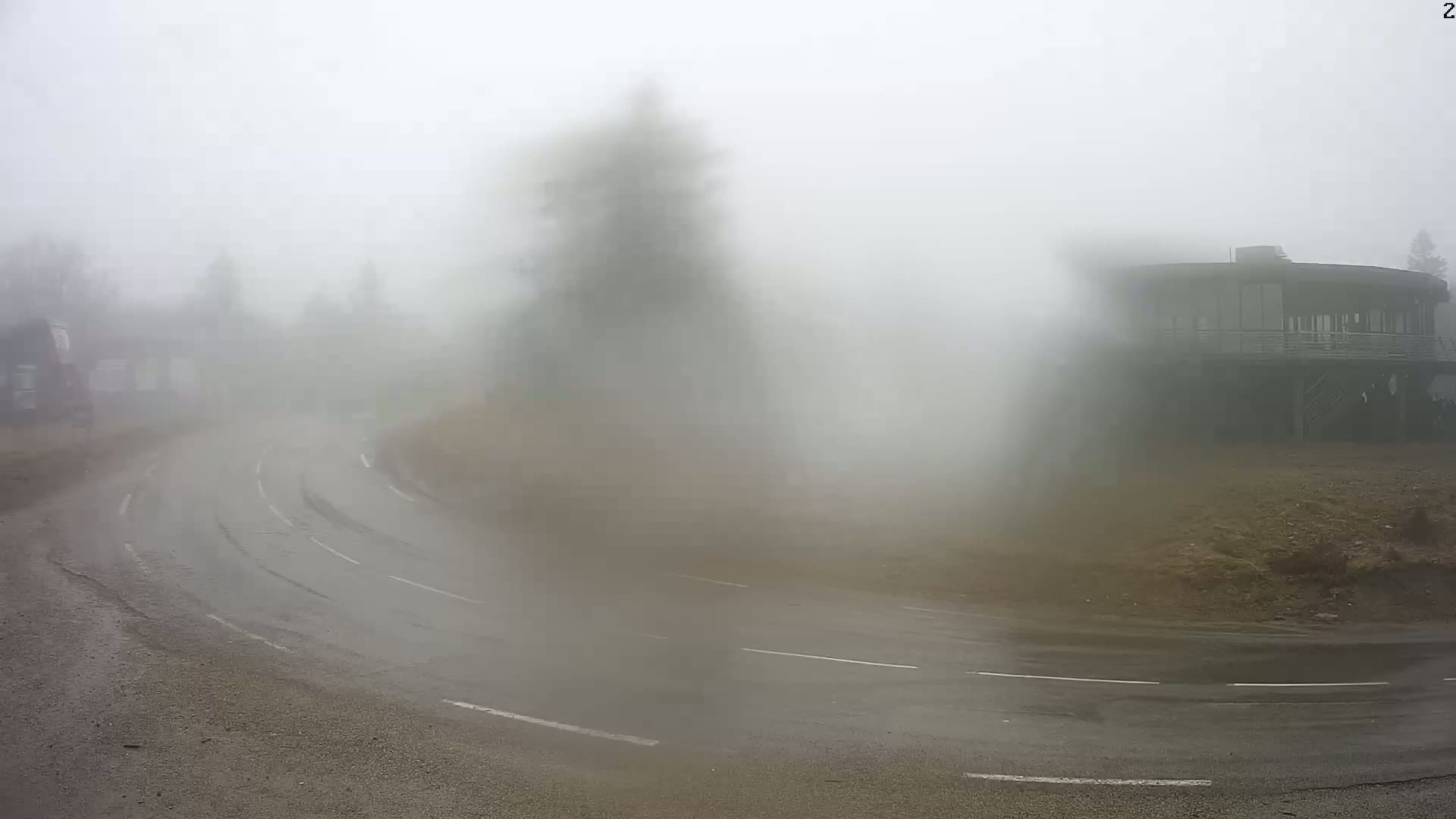 A curving road is shrouded in dense fog, with a large, circular building partially visible in the background.