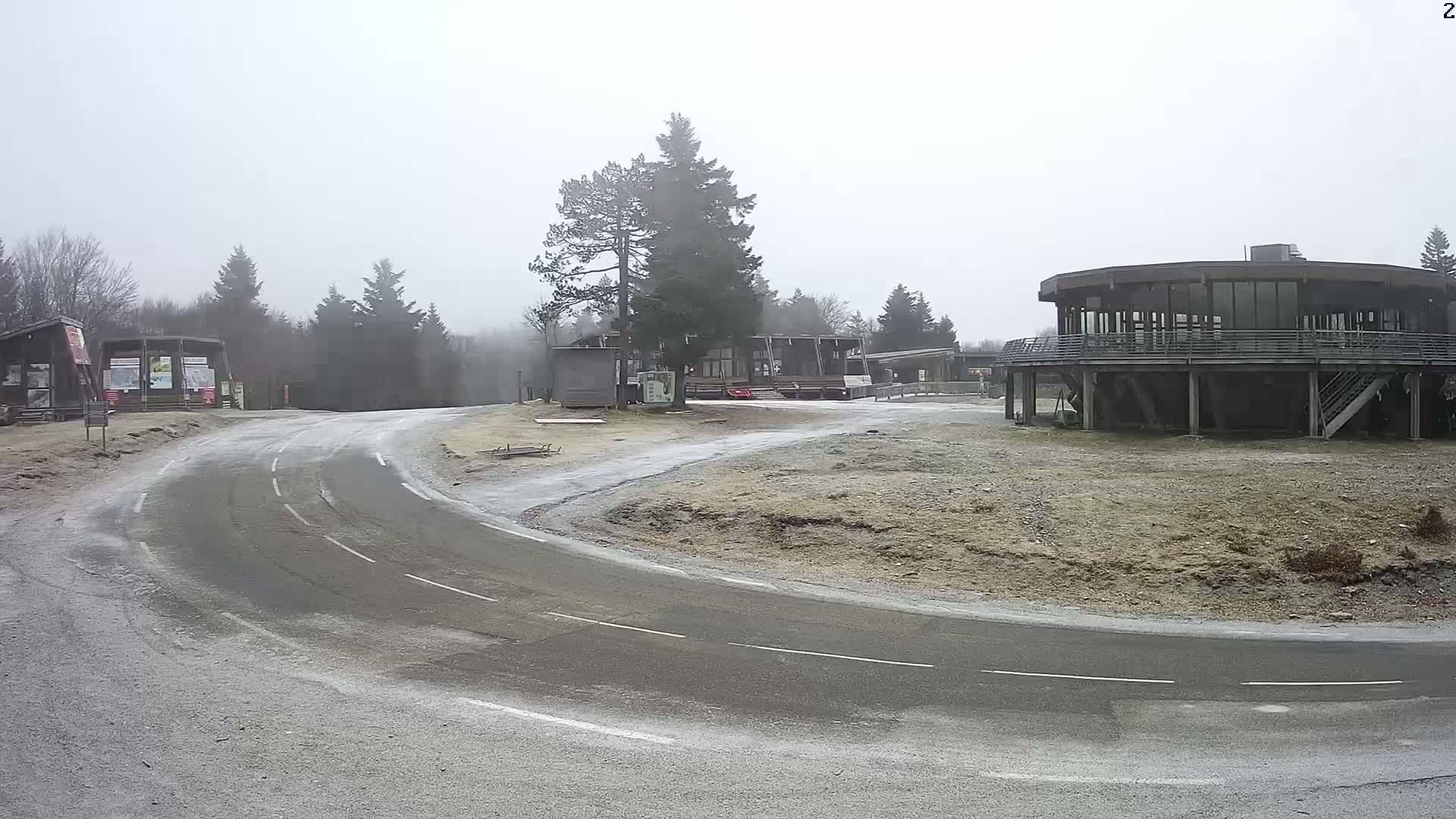 A curved road leads to a cluster of buildings in a foggy, cold setting with frost on the ground.