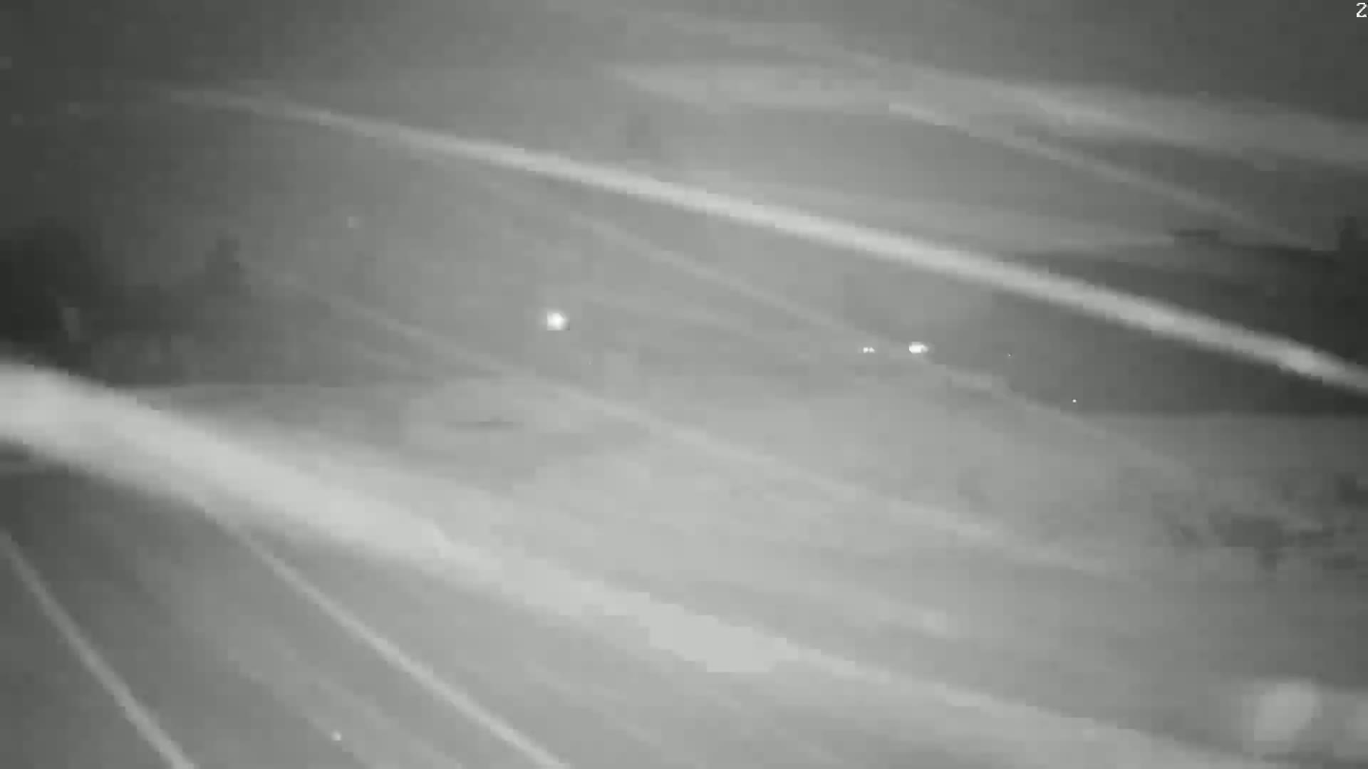 A blurry nighttime image shows a road with faint headlights of distant vehicles and streaks of light suggesting motion blur or snow.