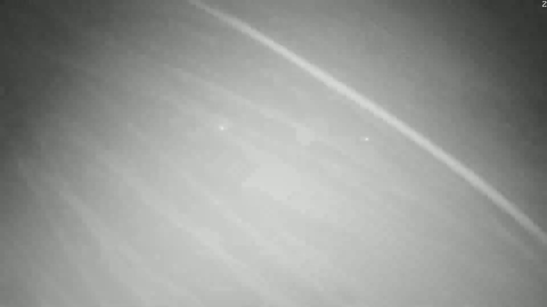 A grayscale image shows a blurry, hazy view of a planet's atmosphere with faint, bright streaks and two small, brighter spots.