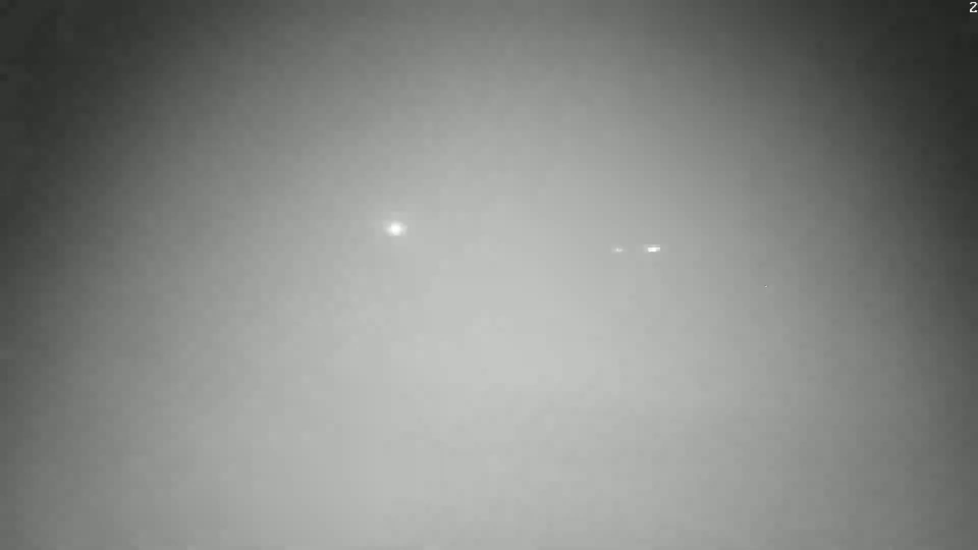 A hazy, gray outdoor scene shows several faint lights in the distance.