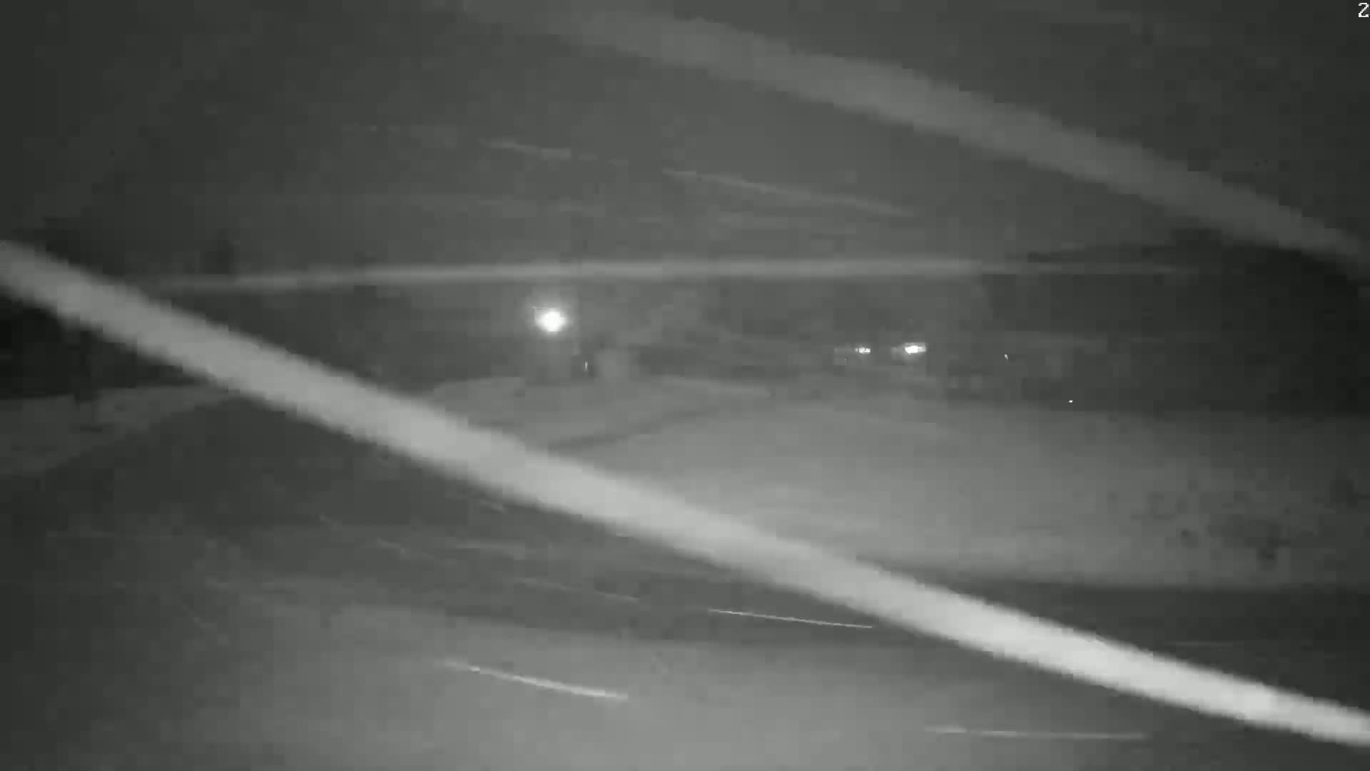 A nighttime, snowy scene shows a mostly empty road with faint light sources in the distance.