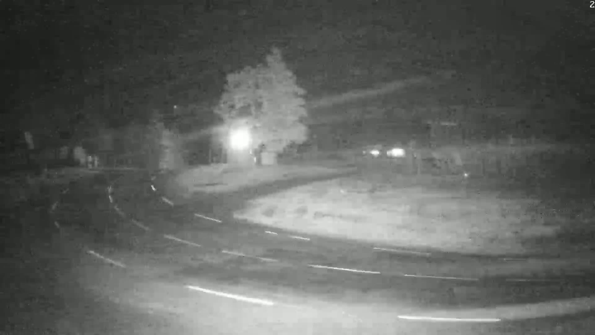A nighttime, low-light image shows a roundabout with vehicle light trails indicating moving cars under possibly snowy or icy conditions.