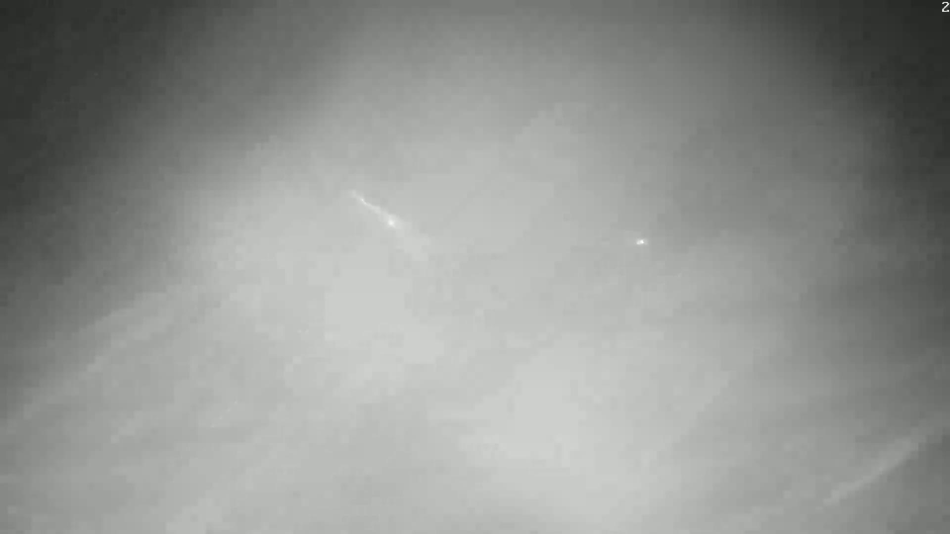 A grayscale image shows two faint streaks of light in an overcast sky.