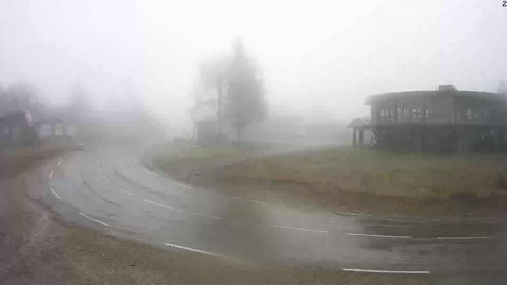 A curving road is wet and shrouded in heavy fog, with a few buildings barely visible in the distance.