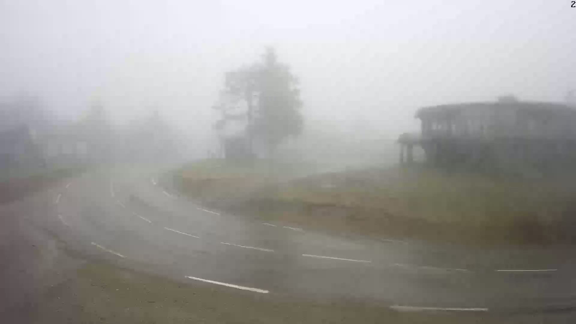 A winding road curves through a foggy, rainy landscape with a few buildings and trees barely visible in the distance.