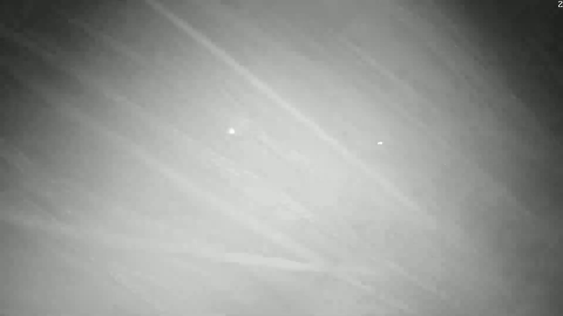 A grayscale image shows a cloudy sky with two faint, distant lights.