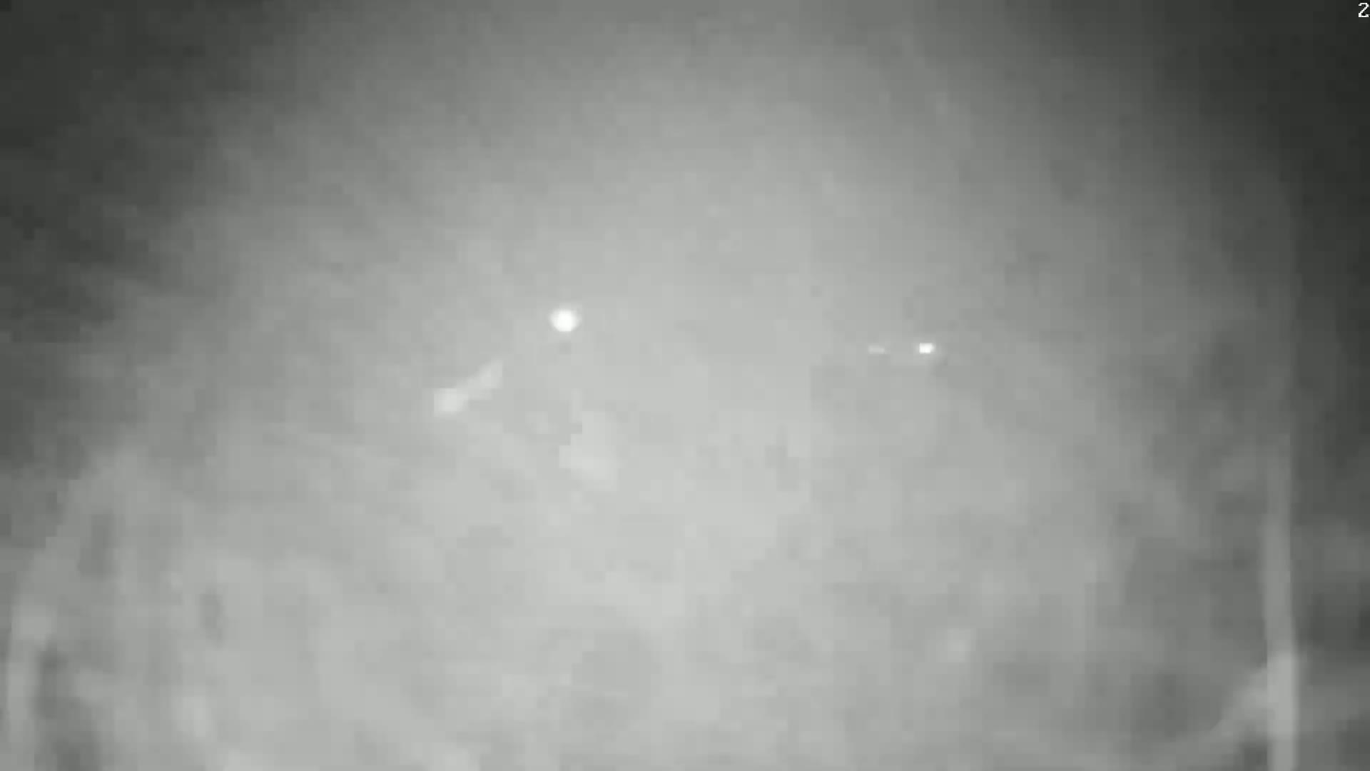 A blurry, nighttime image shows indistinct shapes and faint lights in foggy or hazy conditions.