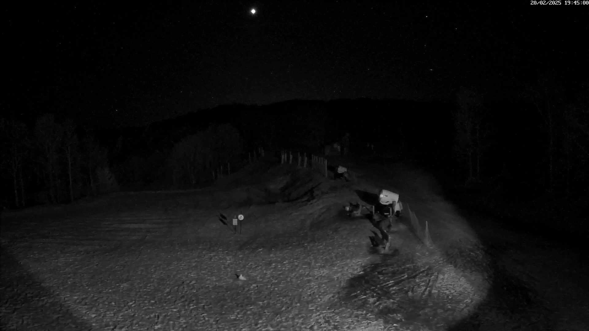 A nighttime, snow-covered landscape is visible under a starry sky, featuring several pieces of machinery near a treeline.