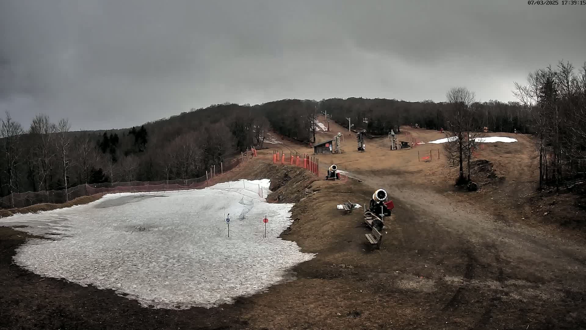 A snowmaking operation at a ski slope under an overcast sky.
