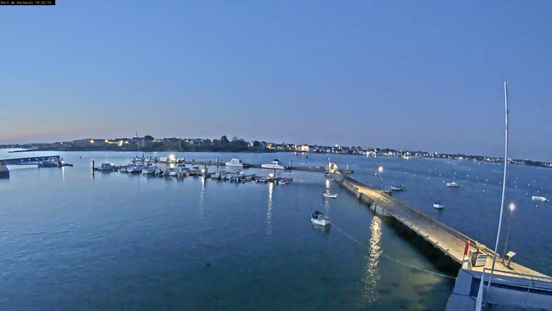 Numerous boats are moored in a calm harbor at twilight, with a town visible in the distance.