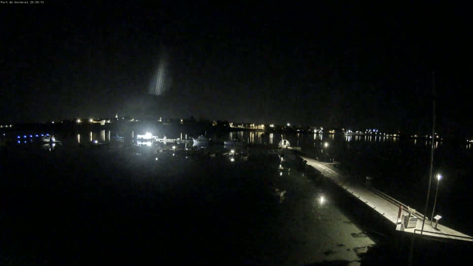 A nighttime view of a harbor with boats and a pier, under a clear, dark sky.