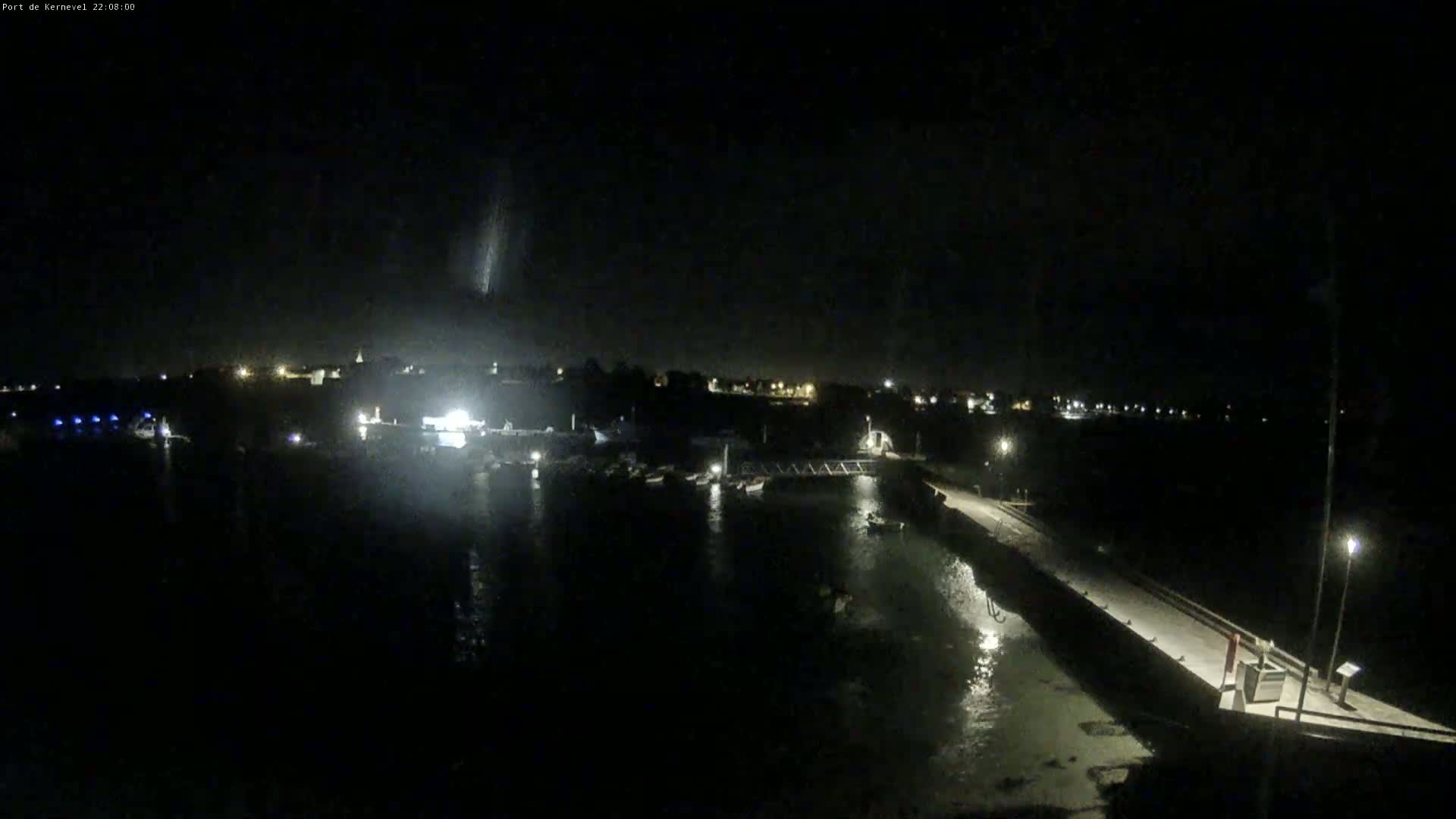 A nighttime view of a harbor with boats moored at a pier under a dark sky.