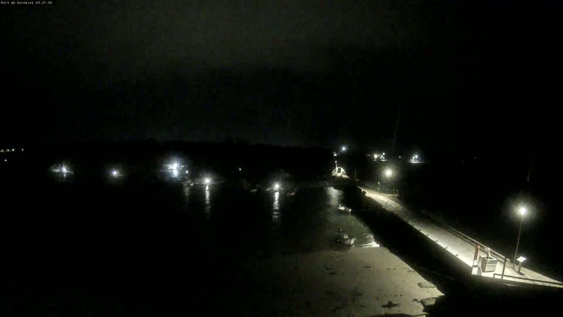 A nighttime view of a harbor with several boats moored, lit by faint lights against a dark, overcast sky.