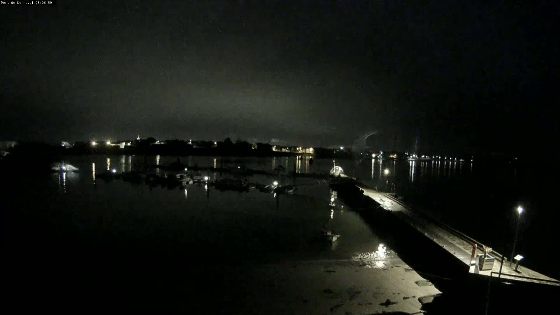 A nighttime view of a harbor with boats docked, illuminated by dim lights under a dark, cloudy sky.