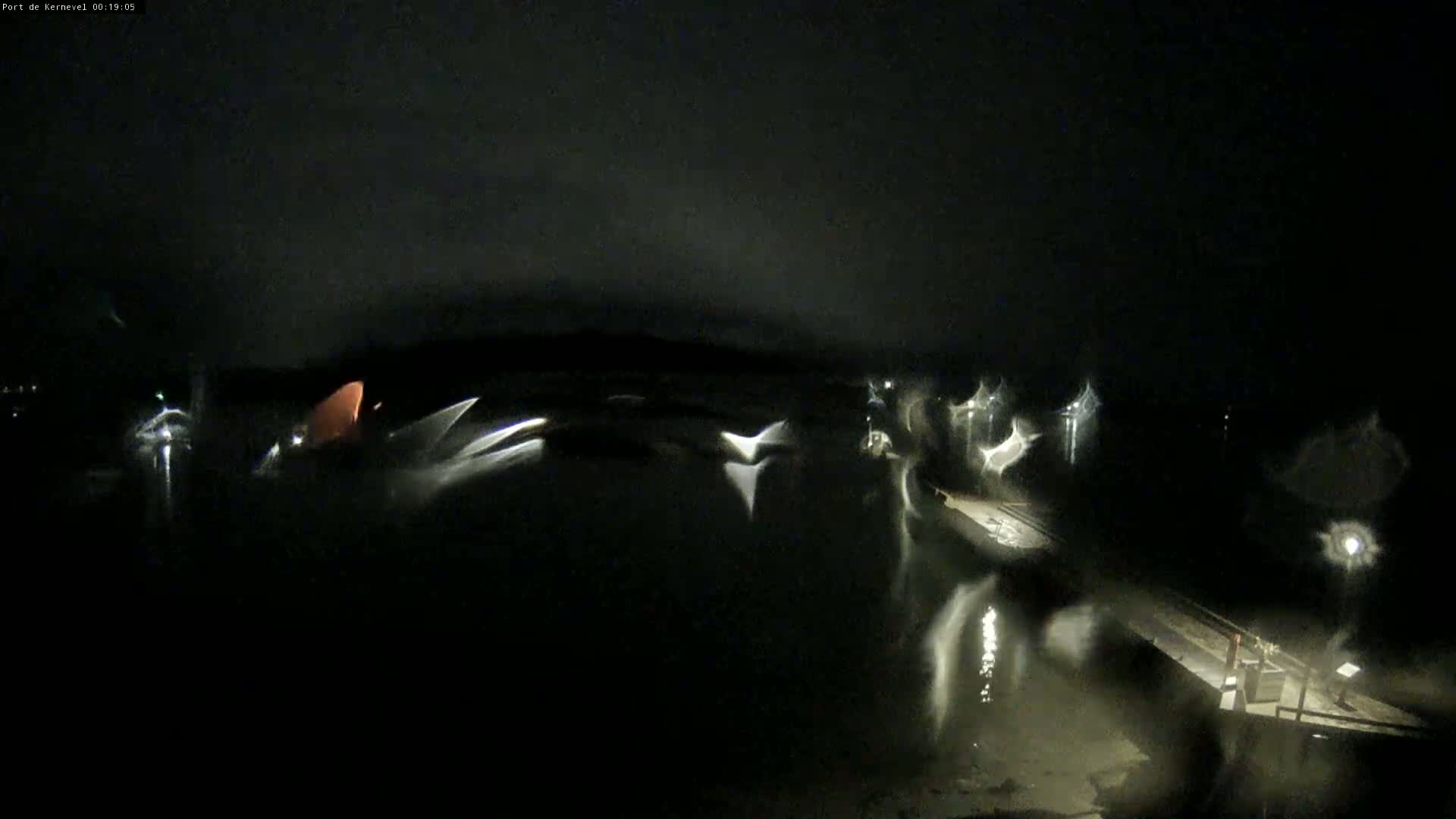 A nighttime, blurry view of a dark body of water with faint lights reflecting on the surface near a dock.