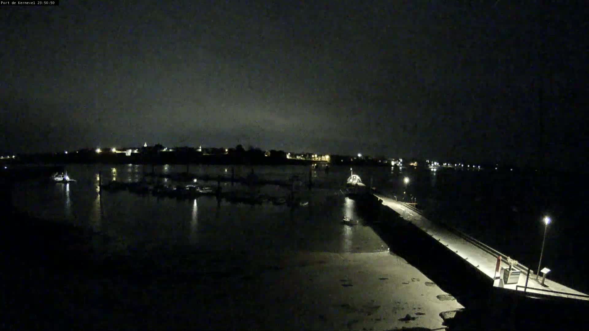 A nighttime view of a harbor with boats docked, illuminated by dim lights under a dark sky.