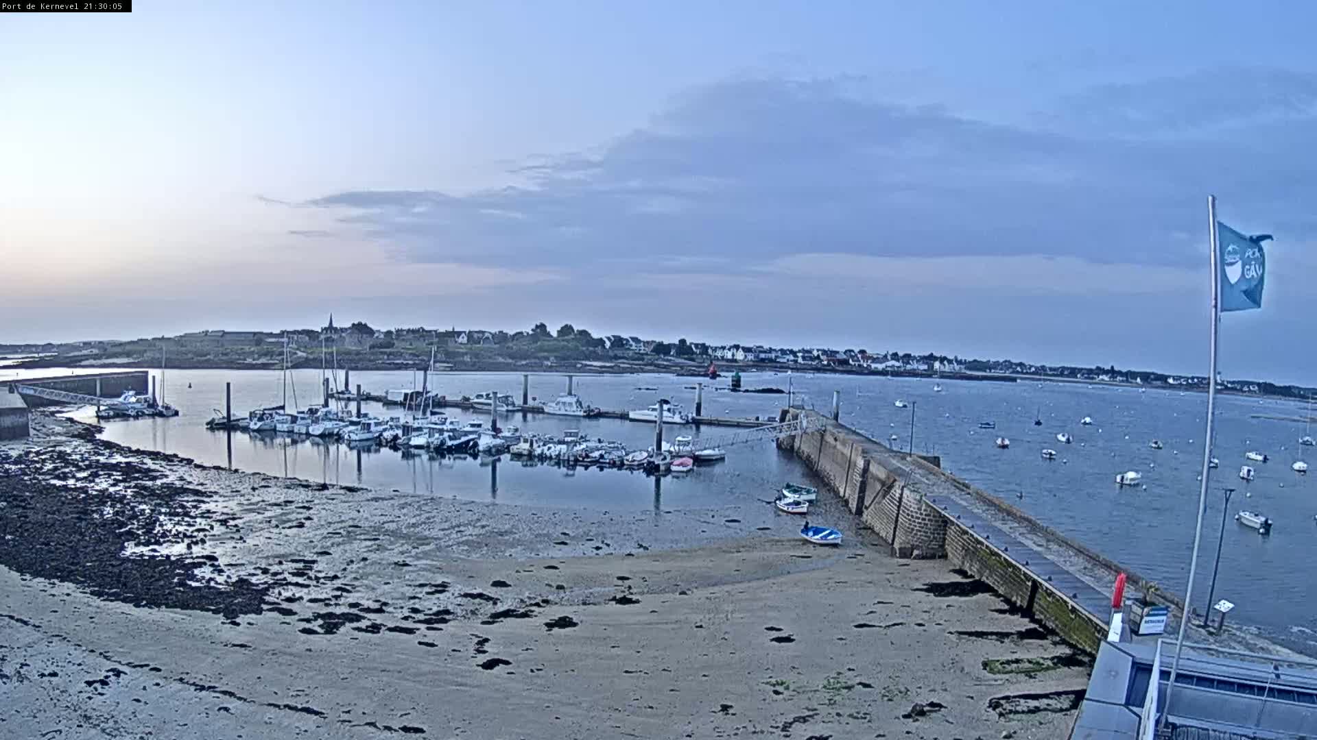 A calm harbor filled with numerous boats at low tide under a mostly cloudy, light blue sky.