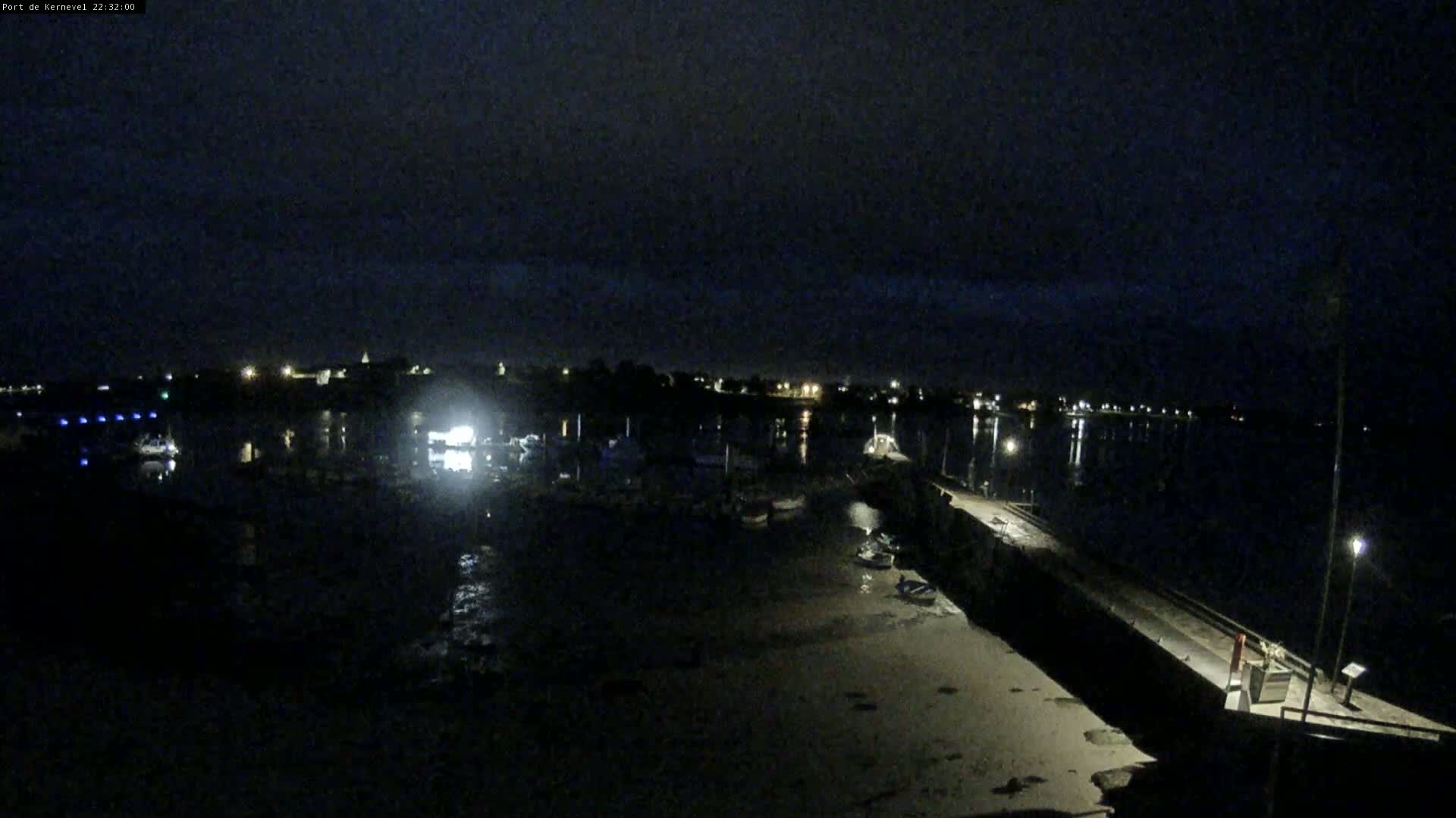 A nighttime view of a harbor with boats and a pier, under a dark sky.