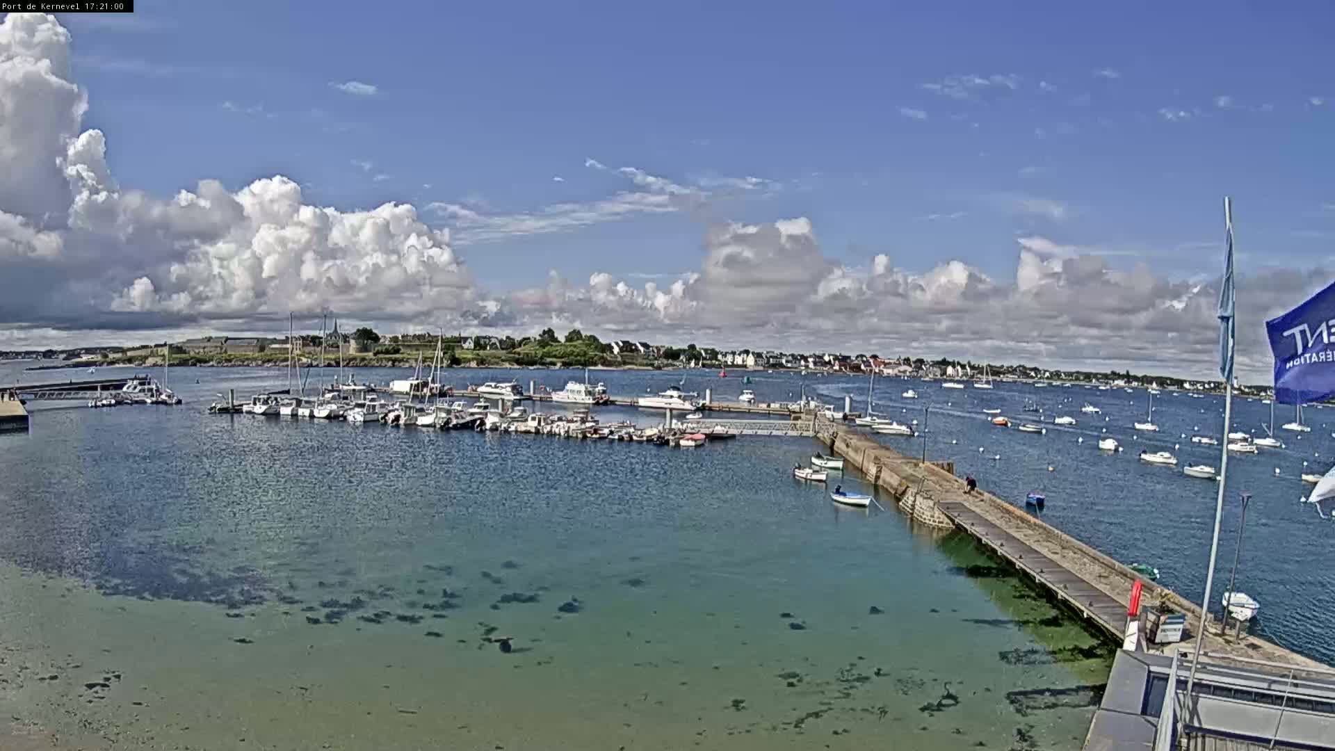 A marina filled with numerous boats is situated under a partly cloudy sky, with additional boats visible in the surrounding bay.