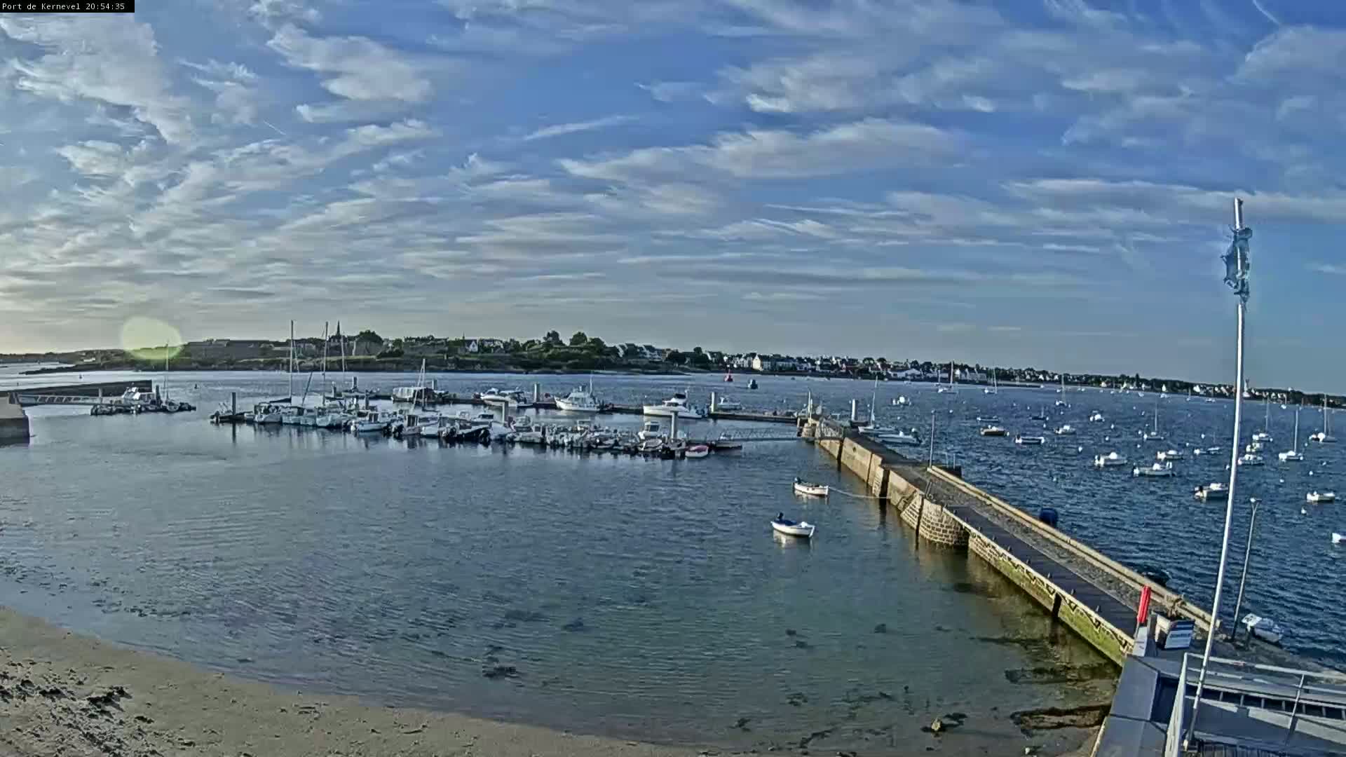 A marina filled with numerous boats is situated on calm, blue water under a mostly clear sky with scattered clouds.
