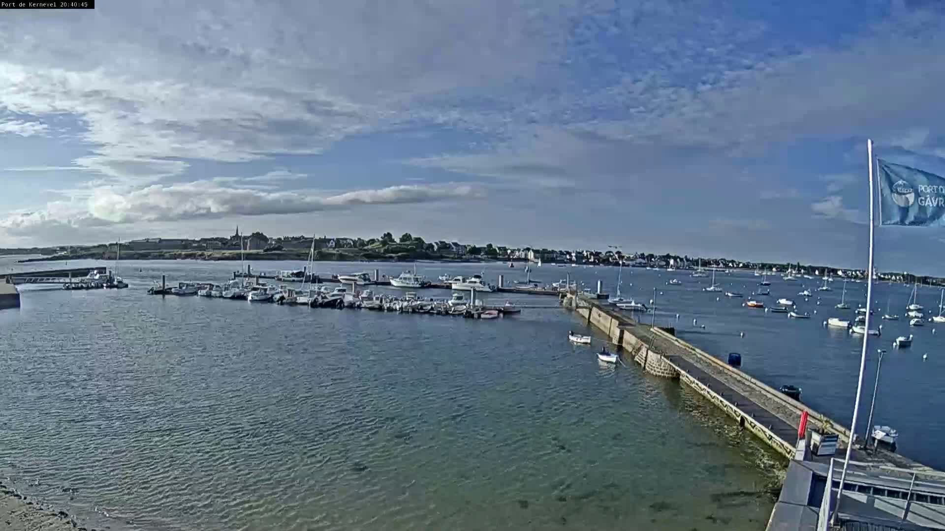 A harbor filled with numerous boats is seen under a partly cloudy sky.