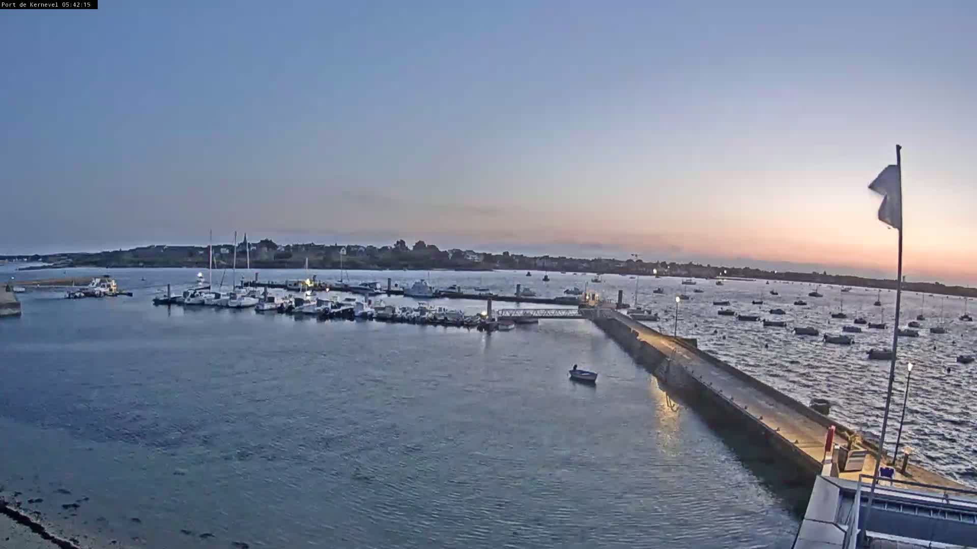 A harbor filled with numerous boats is shown at sunset under a clear sky.