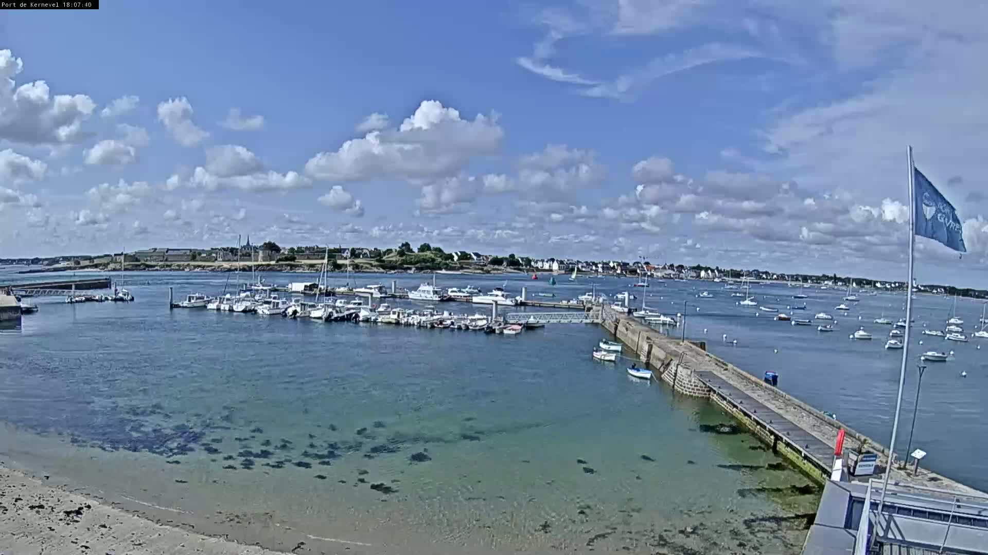 A harbor filled with numerous boats is seen under a partly cloudy sky.