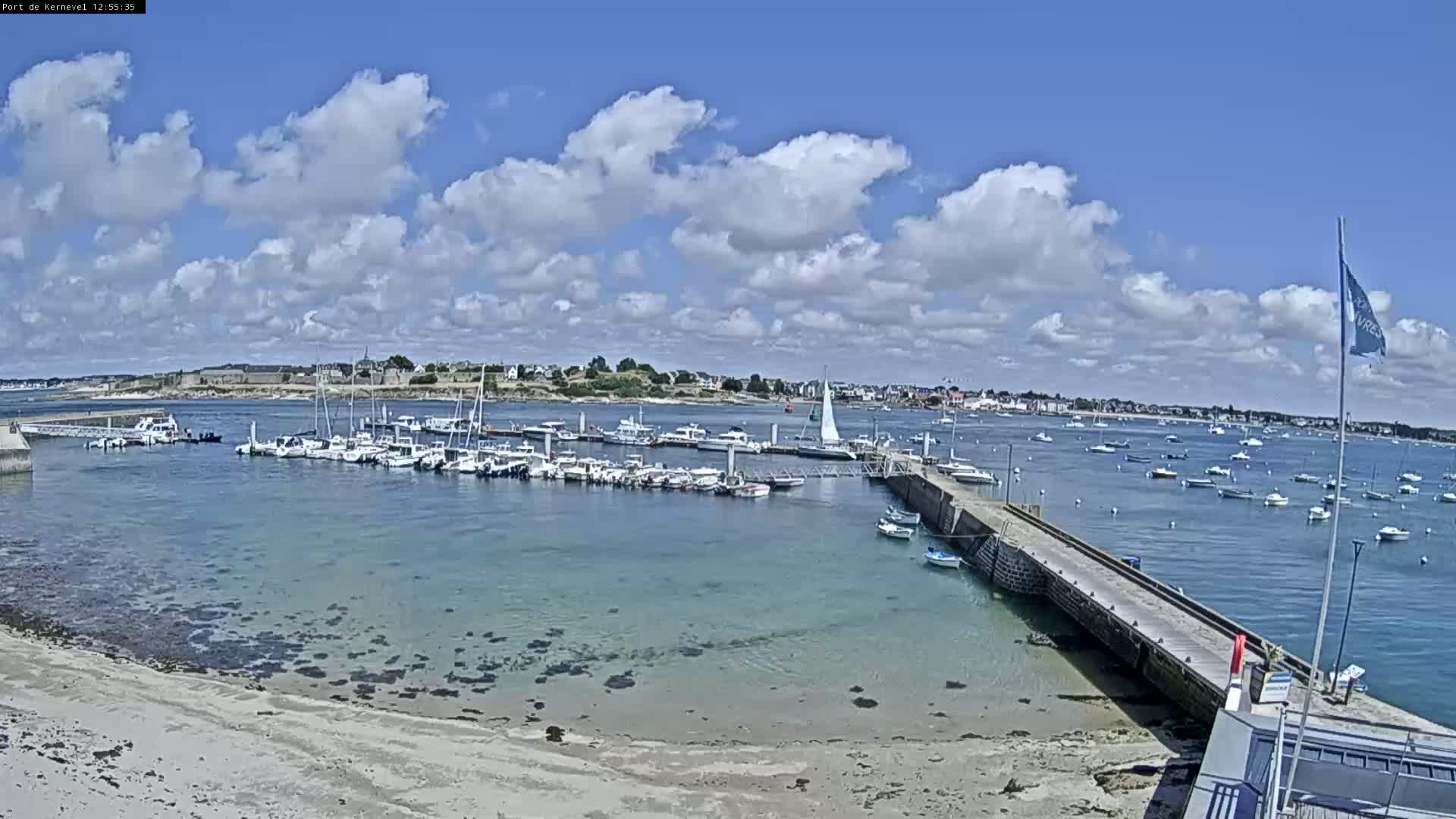 A marina filled with numerous boats is situated on a calm, clear body of water under a partly cloudy sky.
