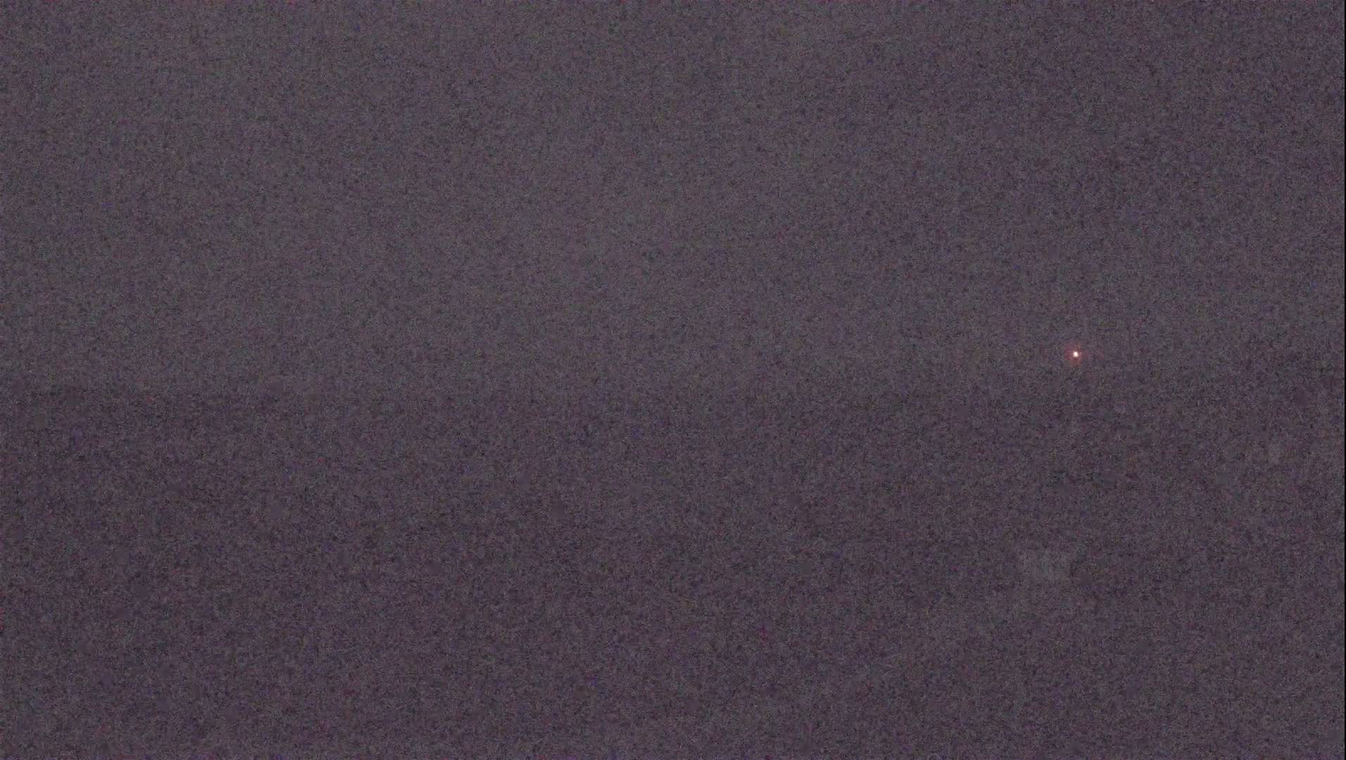 A dark, possibly nighttime, scene shows a single, faint reddish light in the distance.