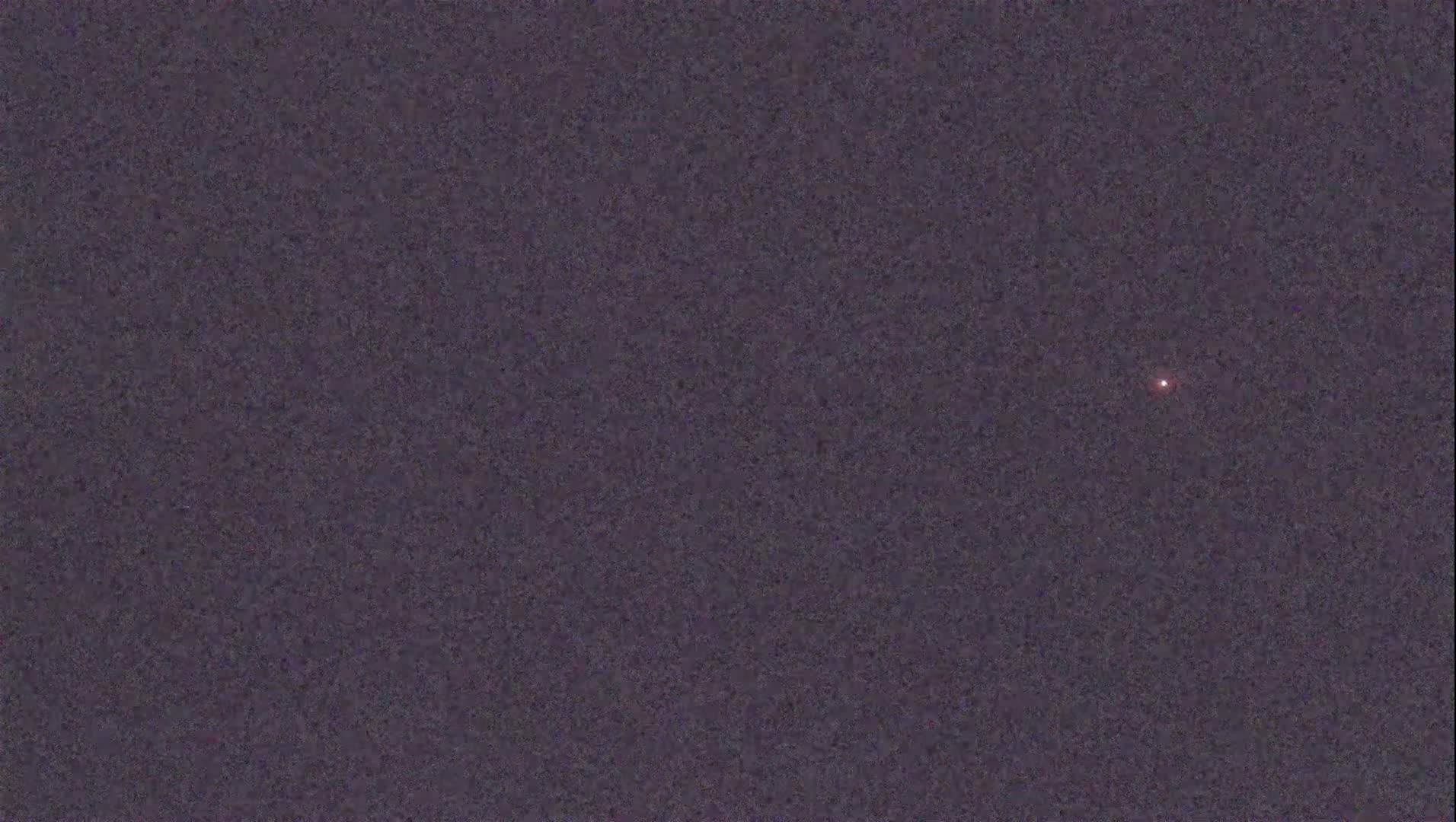 A single, faint, reddish light is visible against a dark, textured night sky.
