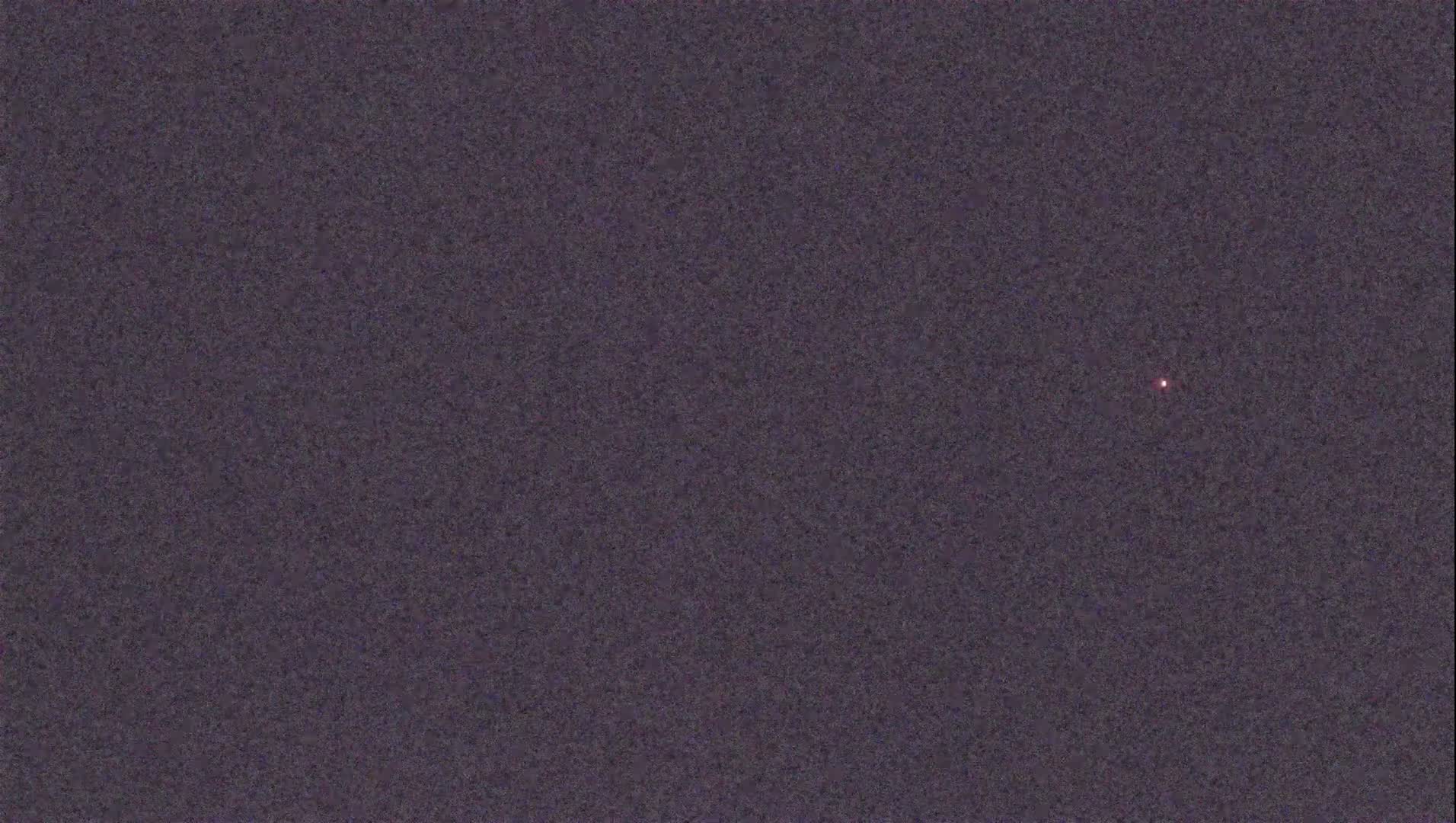 A single, small, red light is visible against a dark, textured background.