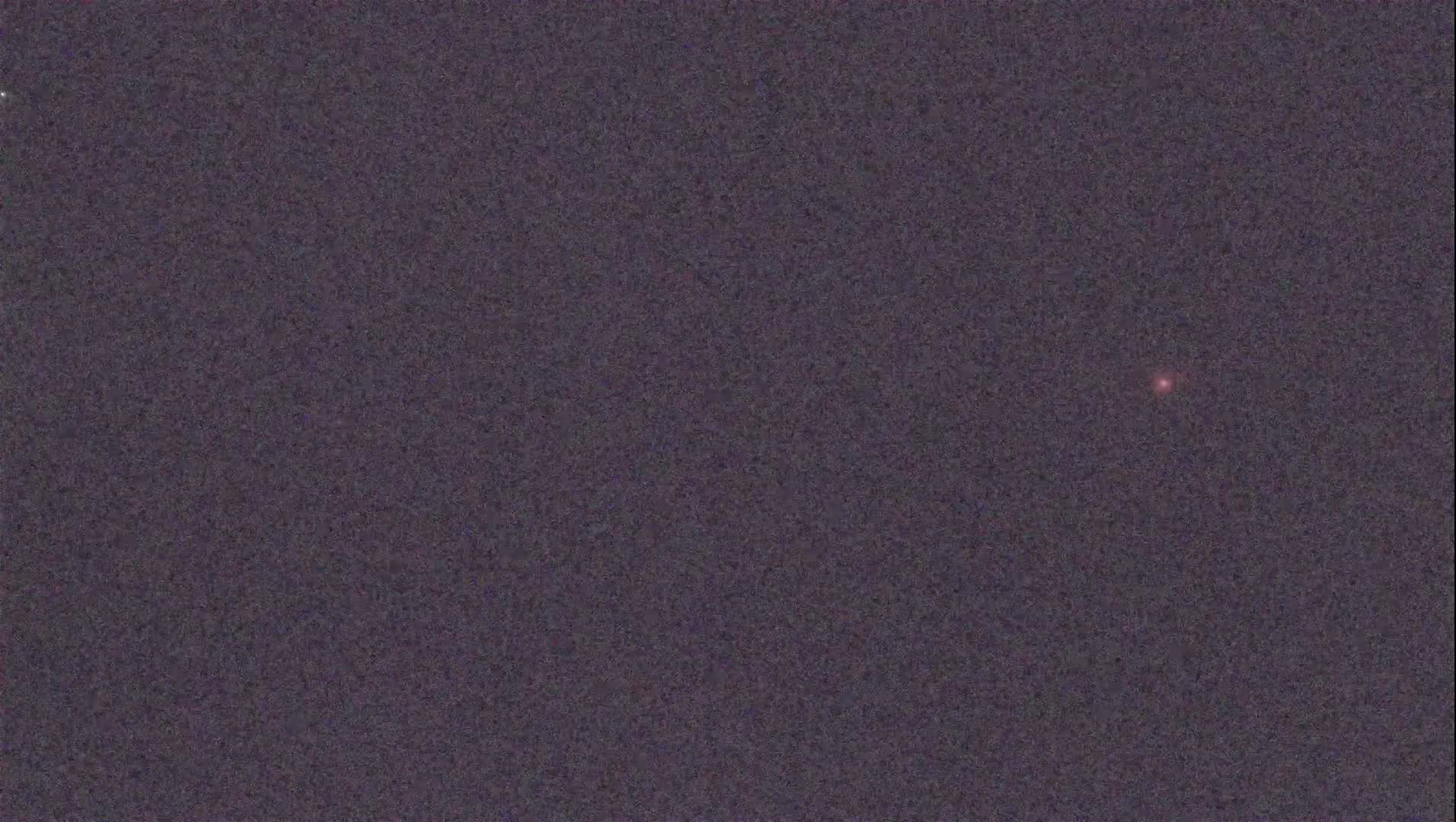 A single, faint, reddish light is visible in a dark, night sky.