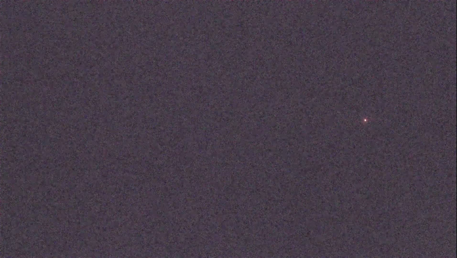 A single, small, reddish light is visible against a dark, textured background under a night sky.