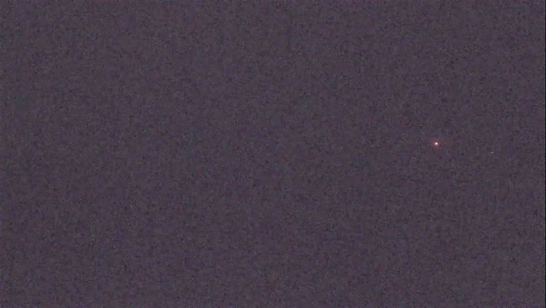 A single, small, reddish light is visible in a dark, night sky.