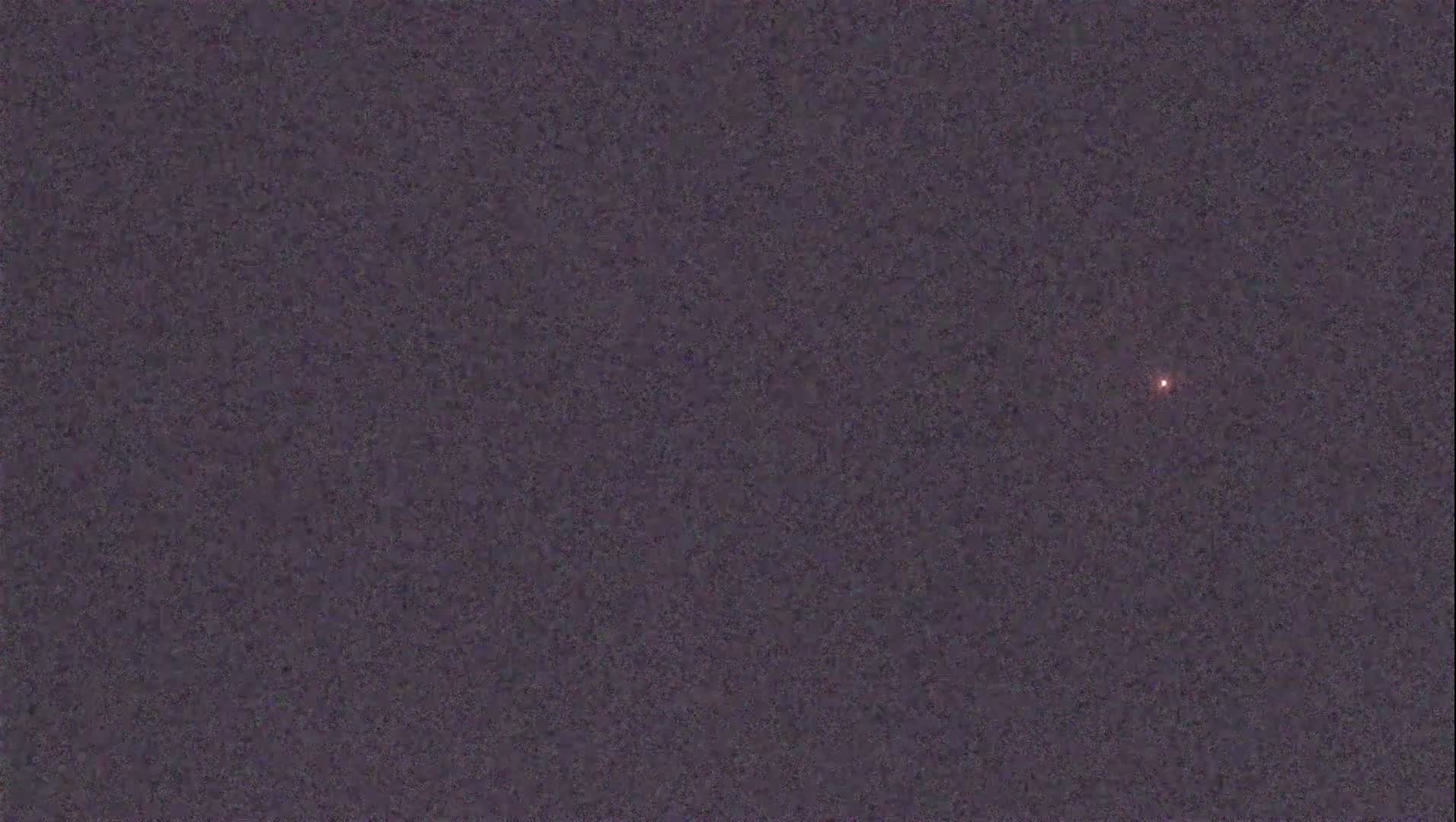 A small, faint, reddish light is visible in a dark, night sky.