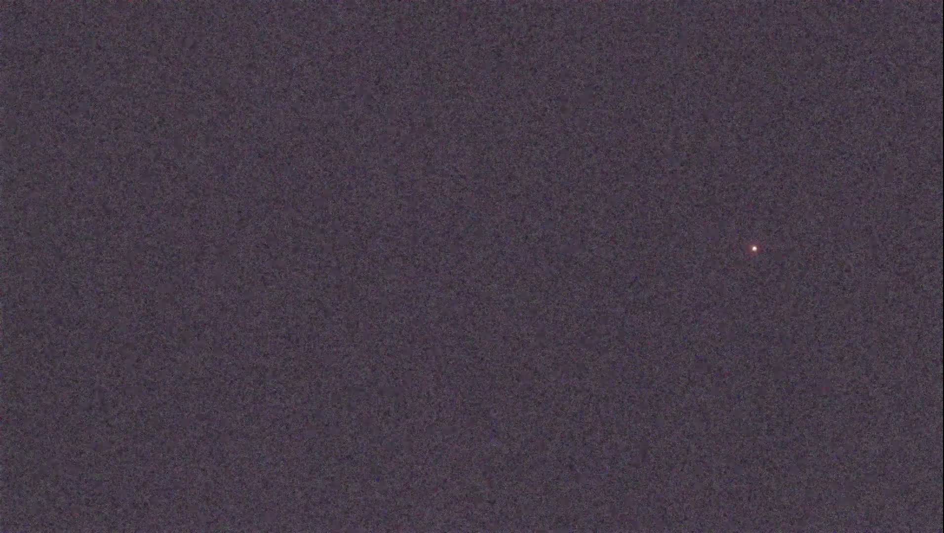 A single, faint, reddish light is visible in a dark, night sky.