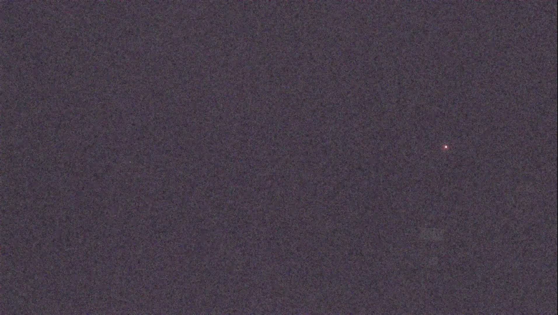 A single, faint, reddish light is visible in a dark, night sky.