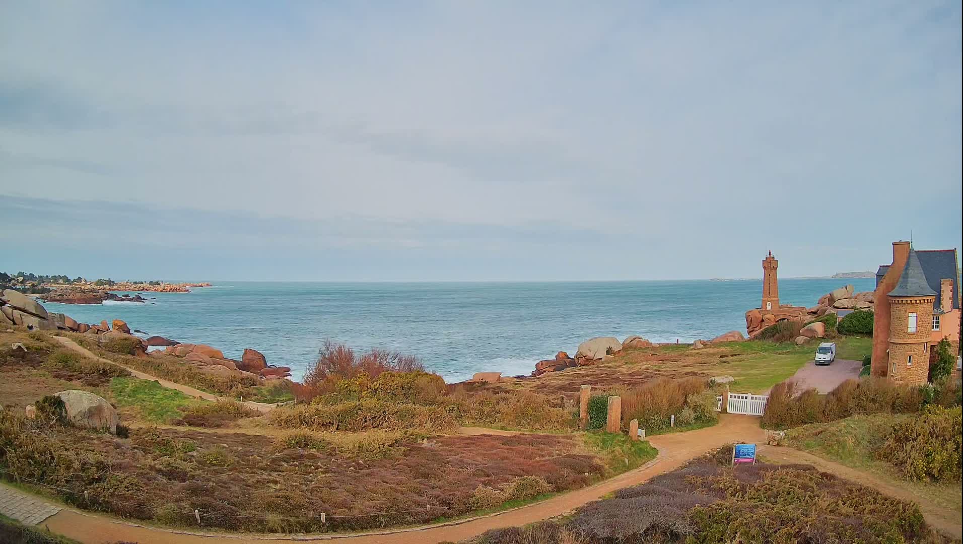 A coastal scene with a lighthouse and a stone house overlooking a calm sea under a cloudy sky.
