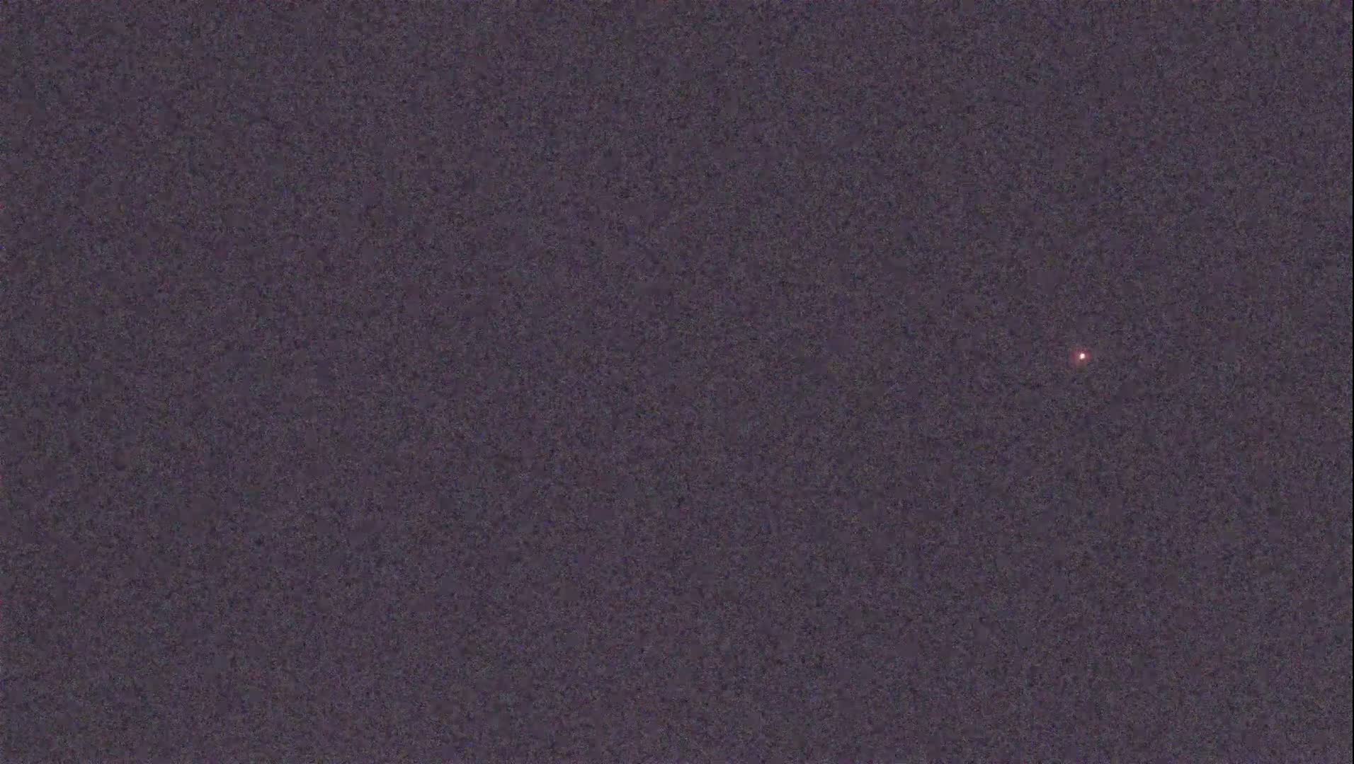 A single, small, reddish light is visible in a dark, textured night sky.
