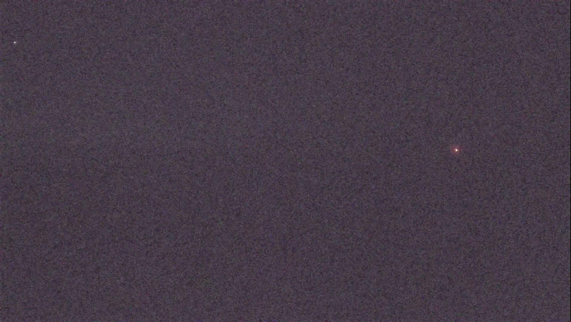 A dark, night sky shows a single, faint, reddish point of light.